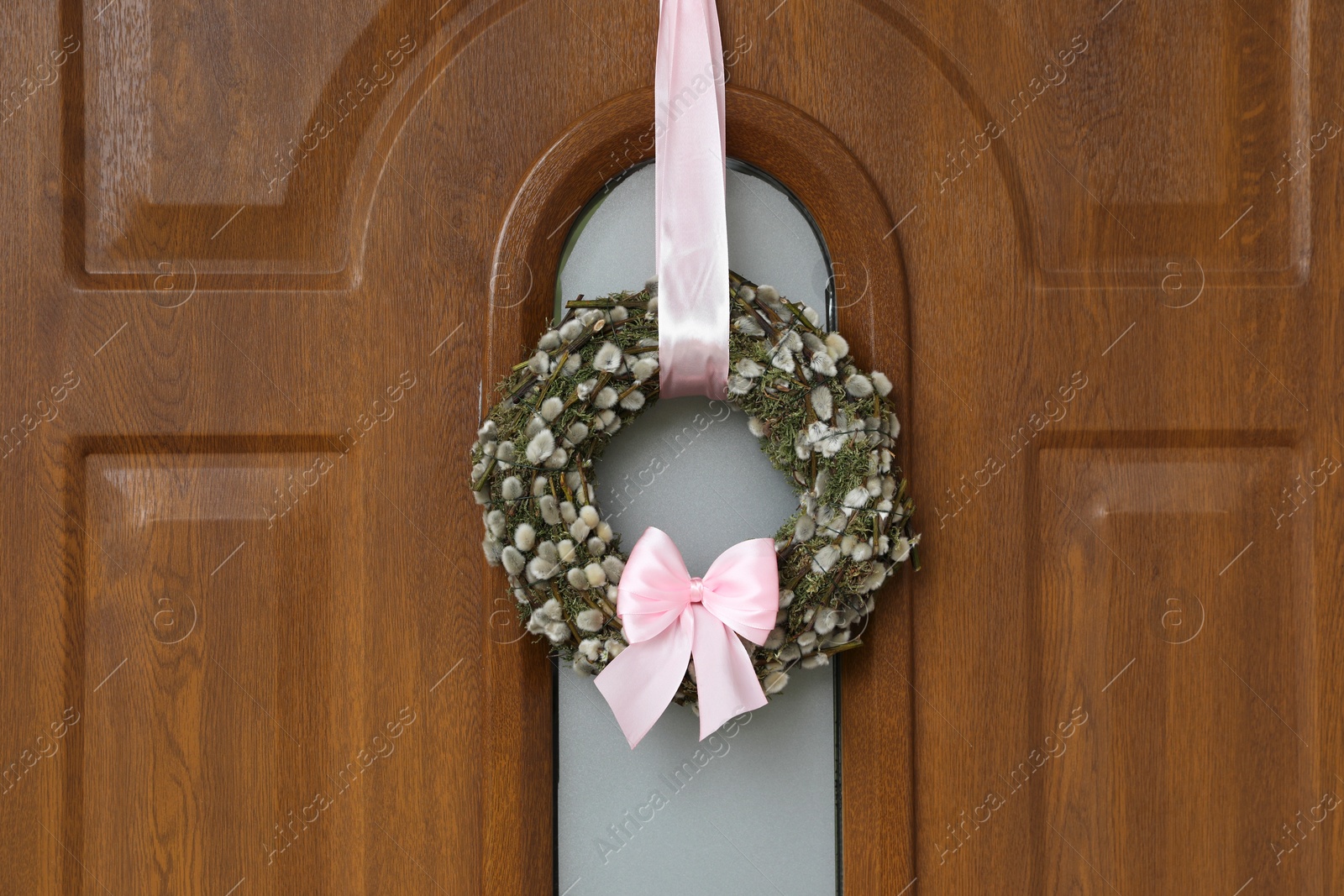 Photo of Wreath made of beautiful willow branches and pink bow on wooden door