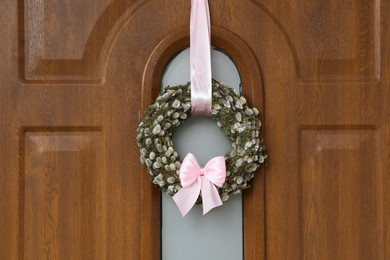 Wreath made of beautiful willow branches and pink bow on wooden door