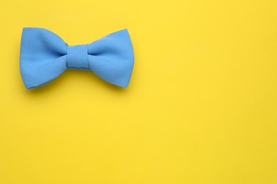 Stylish light blue bow tie on yellow background, top view. Space for text