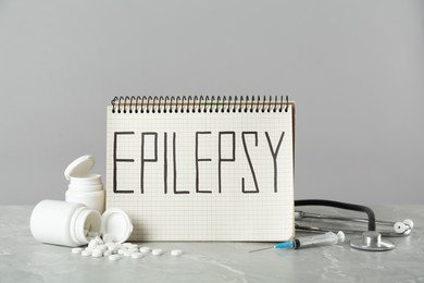 Photo of Notebook with word Epilepsy, stethoscope, pills and syringe on grey marble table