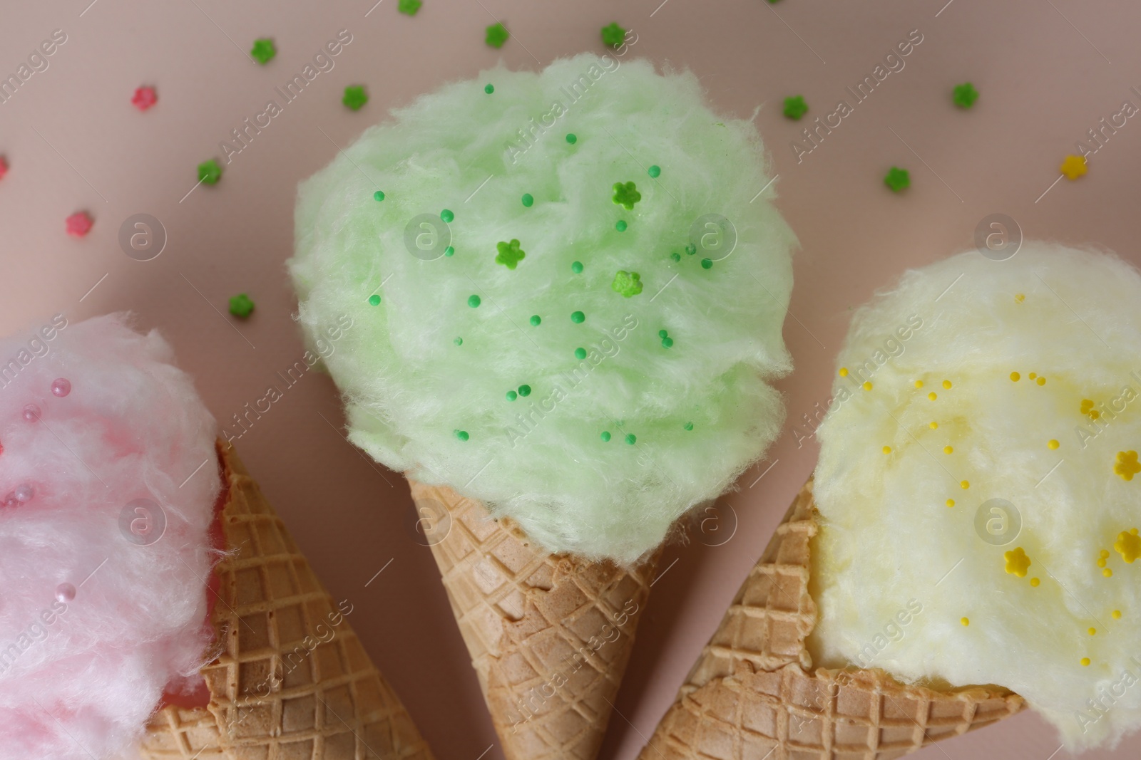 Photo of Sweet cotton candies in waffle cones on beige background, flat lay