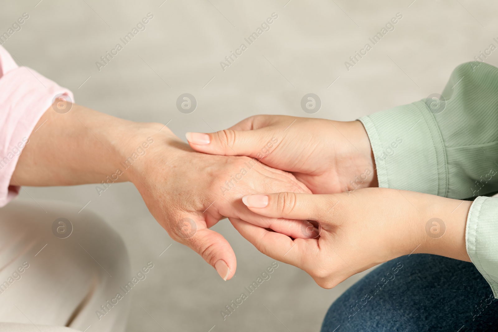 Photo of Young and elderly women holding hands indoors, closeup