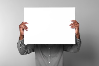 Photo of African American man holding sheet of paper on grey background. Mockup for design