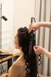 Photo of Hair styling. Hairdresser curling woman's hair in salon, closeup