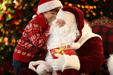 Photo of Santa Claus and little boy near Christmas tree indoors
