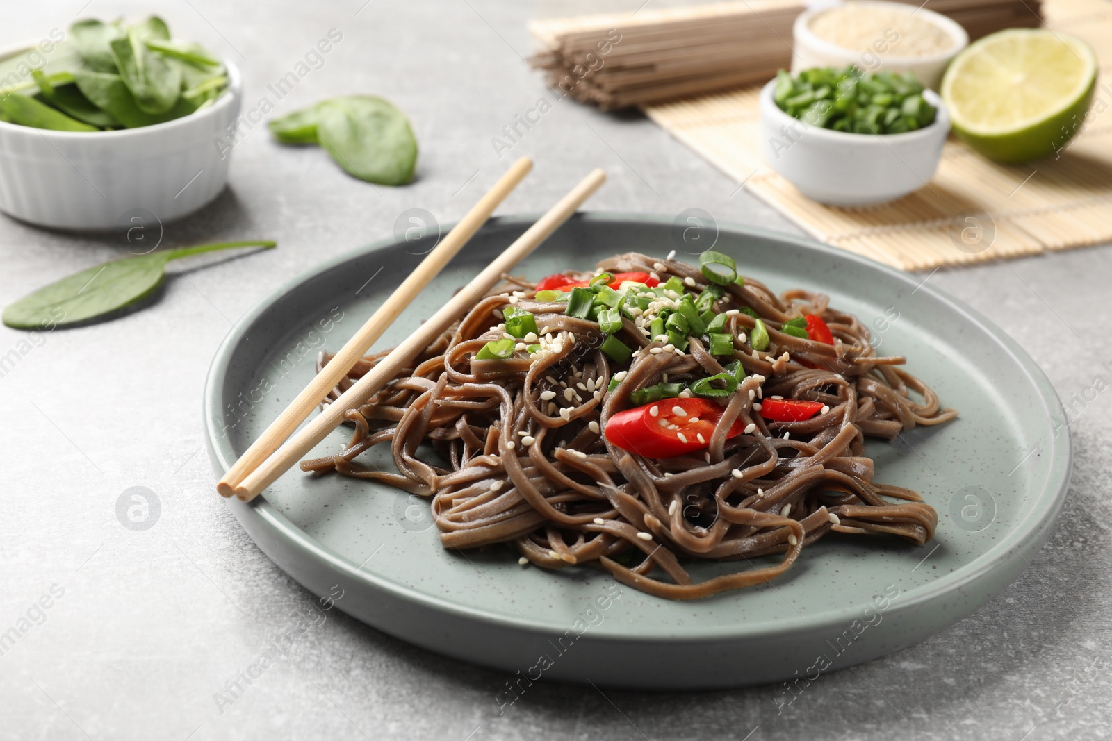 Photo of Tasty buckwheat noodles (soba) with chili pepper, onion and chopsticks on light table