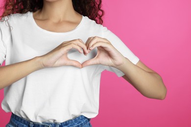Photo of African-American woman making heart with hands on pink background, closeup
