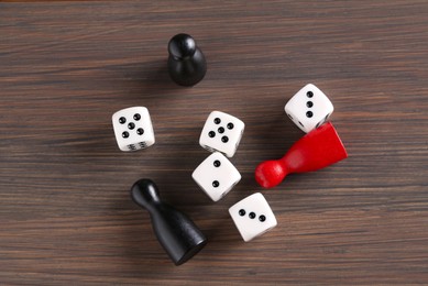 Photo of Many white dices and color game pieces on wooden table, flat lay