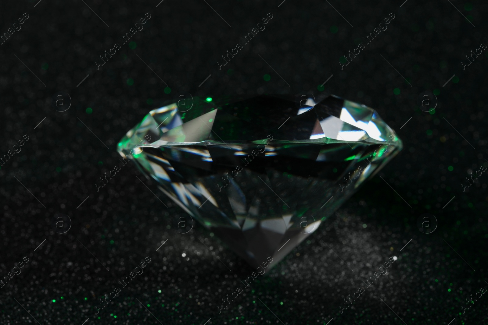 Photo of Beautiful dazzling diamond on dark glitter surface, closeup