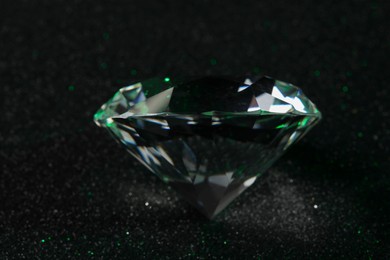 Beautiful dazzling diamond on dark glitter surface, closeup