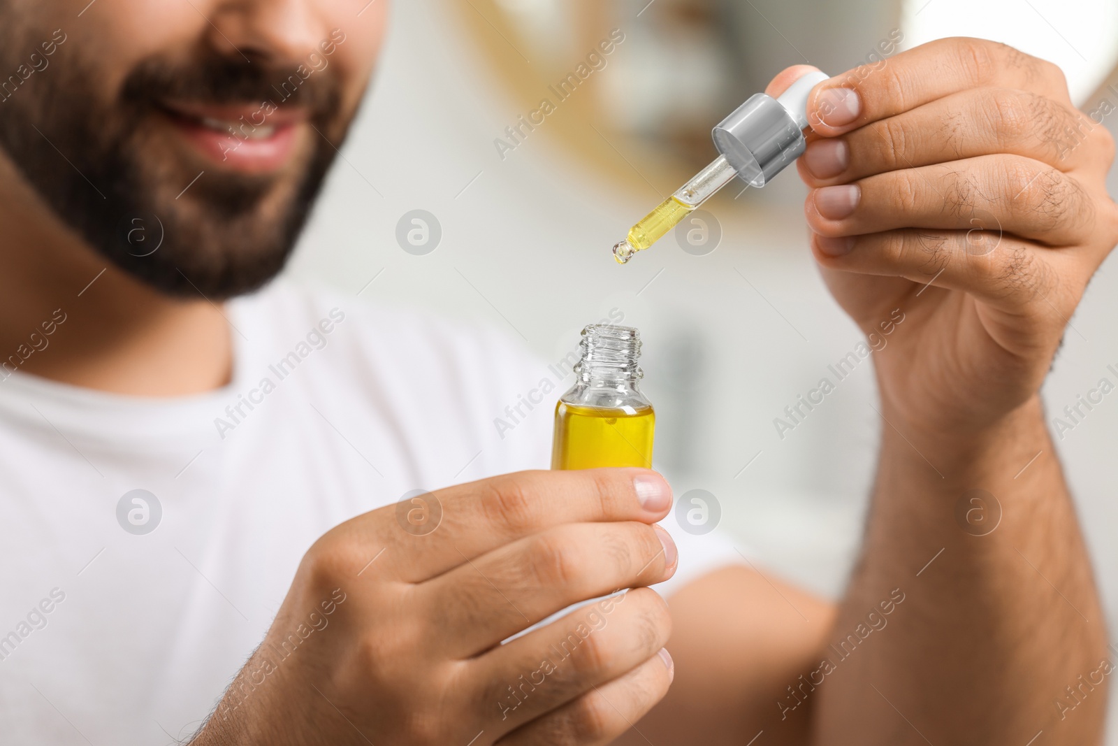 Photo of Young man with cosmetic serum in his hands indoors, closeup
