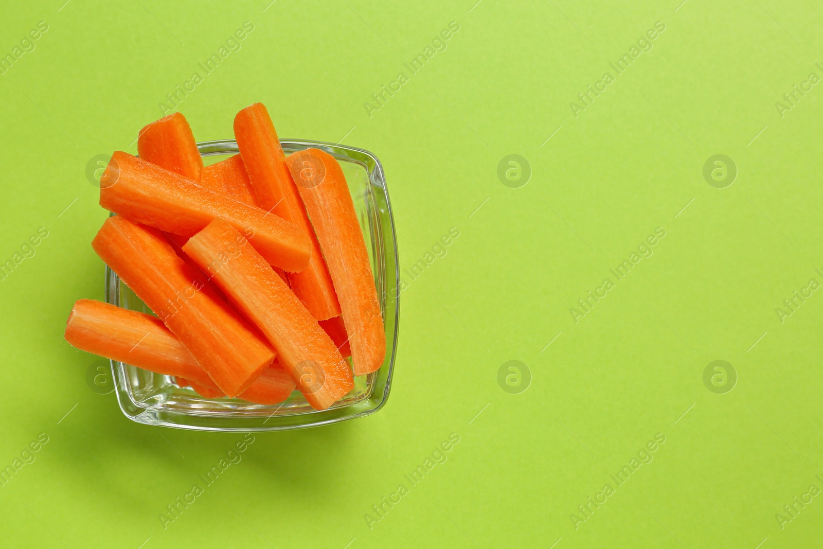 Photo of Cut fresh carrot in bowl and space for text on green background, top view. Finger food