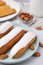 Photo of Delicious eclairs covered with glaze and almonds on white textured table, closeup