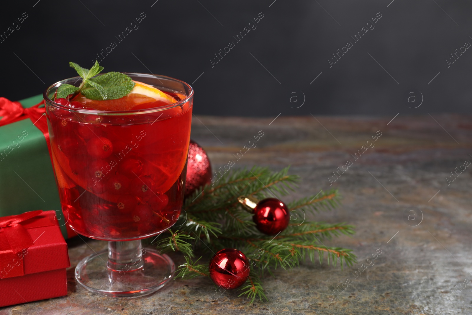Photo of Aromatic Christmas Sangria in glass, gift boxes and festive decor on grey textured table, space for text