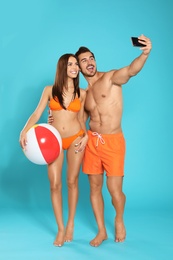 Photo of Young attractive couple in beachwear with ball taking selfie on blue background