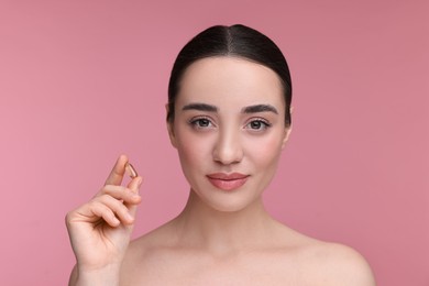 Beautiful young woman with vitamin pill on pink background