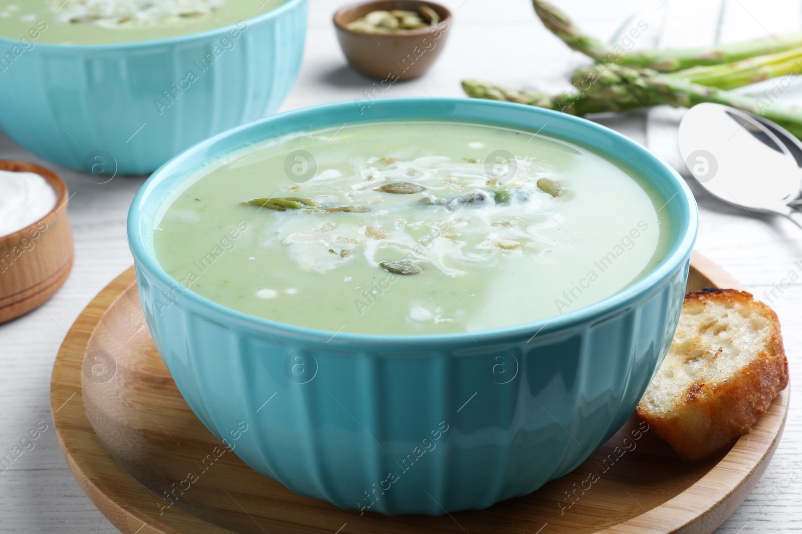 Photo of Bowl of delicious asparagus soup served on white wooden table