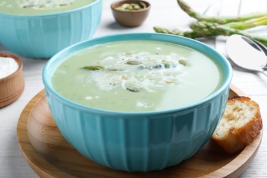 Photo of Bowl of delicious asparagus soup served on white wooden table