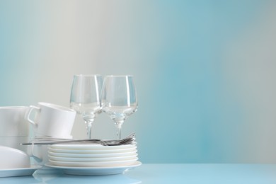 Photo of Set of many clean dishware, cutlery and glasses on light blue table. Space for text