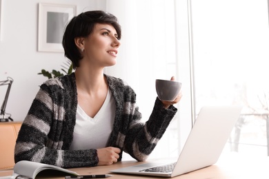 Young woman drinking coffee while working with laptop at desk. Home office