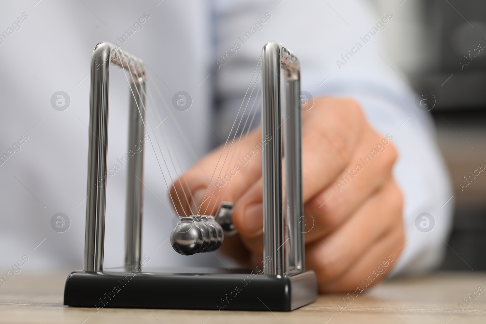 Photo of Man playing with Newton's cradle at table, closeup. Physics law of energy conservation