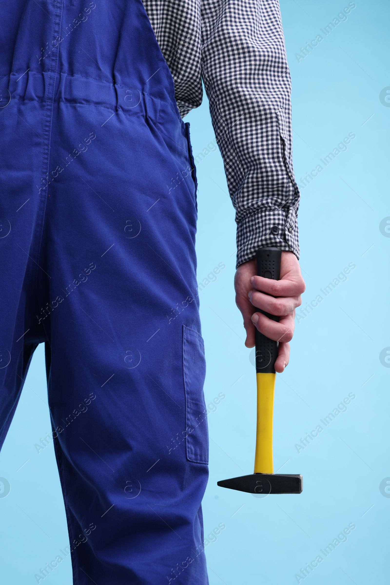 Photo of Professional repairman holding hammer on light blue background, closeup