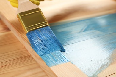 Photo of Worker applying blue paint onto wooden surface, closeup. Space for text