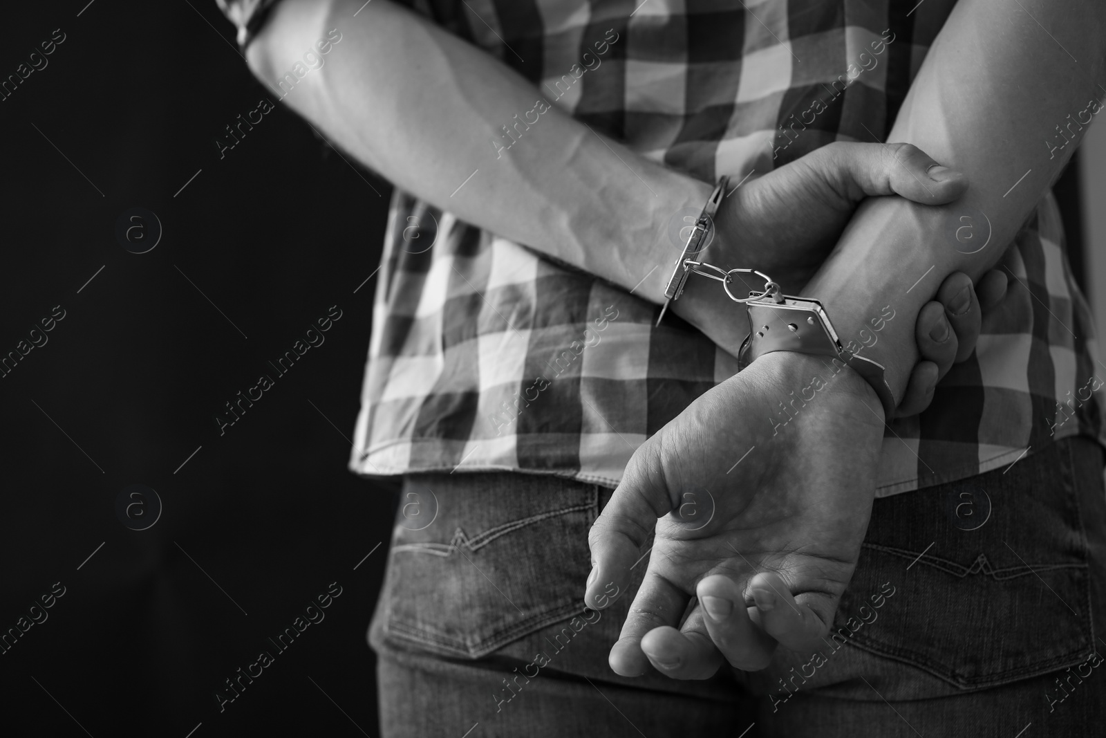 Photo of Criminal detained in handcuffs against dark background, space for text. Black and white effect