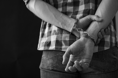 Criminal detained in handcuffs against dark background, space for text. Black and white effect