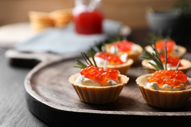 Delicious tartlets with red caviar and cream cheese served on wooden table, closeup. Space for text