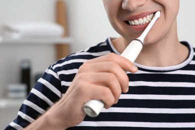 Man brushing his teeth with electric toothbrush in bathroom, closeup