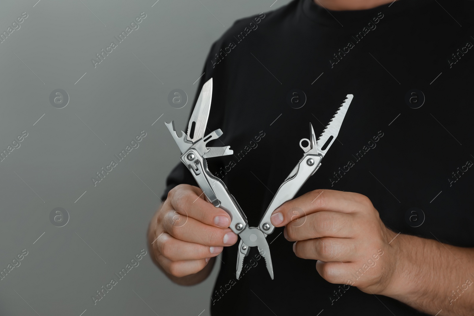 Photo of Man holding multitool on grey background, closeup. Space for text