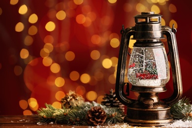 Photo of Beautiful snow globe in vintage lantern on table against blurred Christmas lights. Space for text