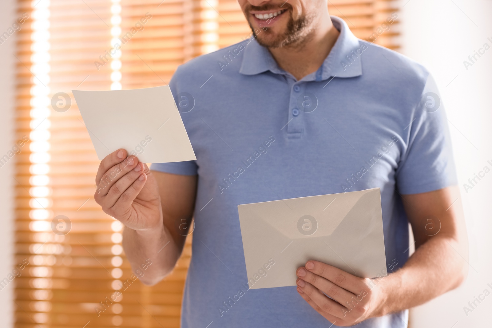 Photo of Man holding envelope with blank greeting card indoors. closeup