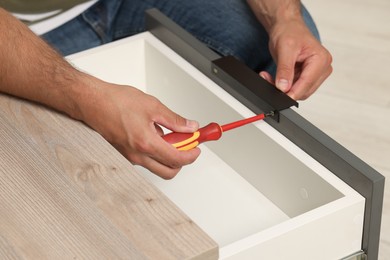 Photo of Man with screwdriver assembling drawer, closeup view