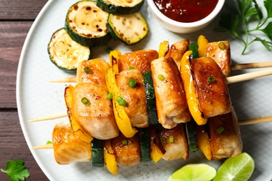 Photo of Delicious chicken shish kebabs with vegetables and sauce on wooden table, top view