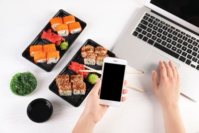 Woman with mobile phone and sushi rolls at table, space for text. Food delivery