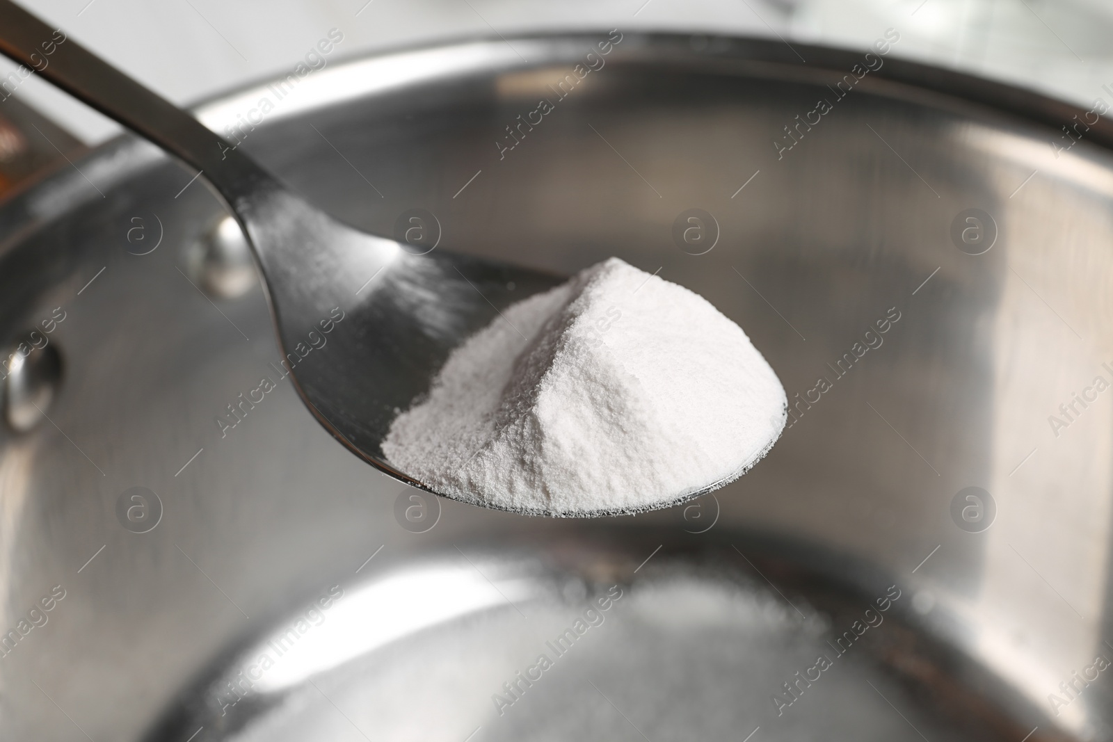 Photo of Spoon with baking soda over saucepan, closeup