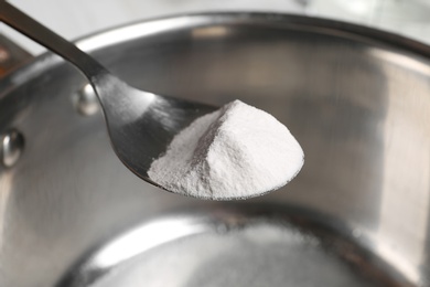 Spoon with baking soda over saucepan, closeup