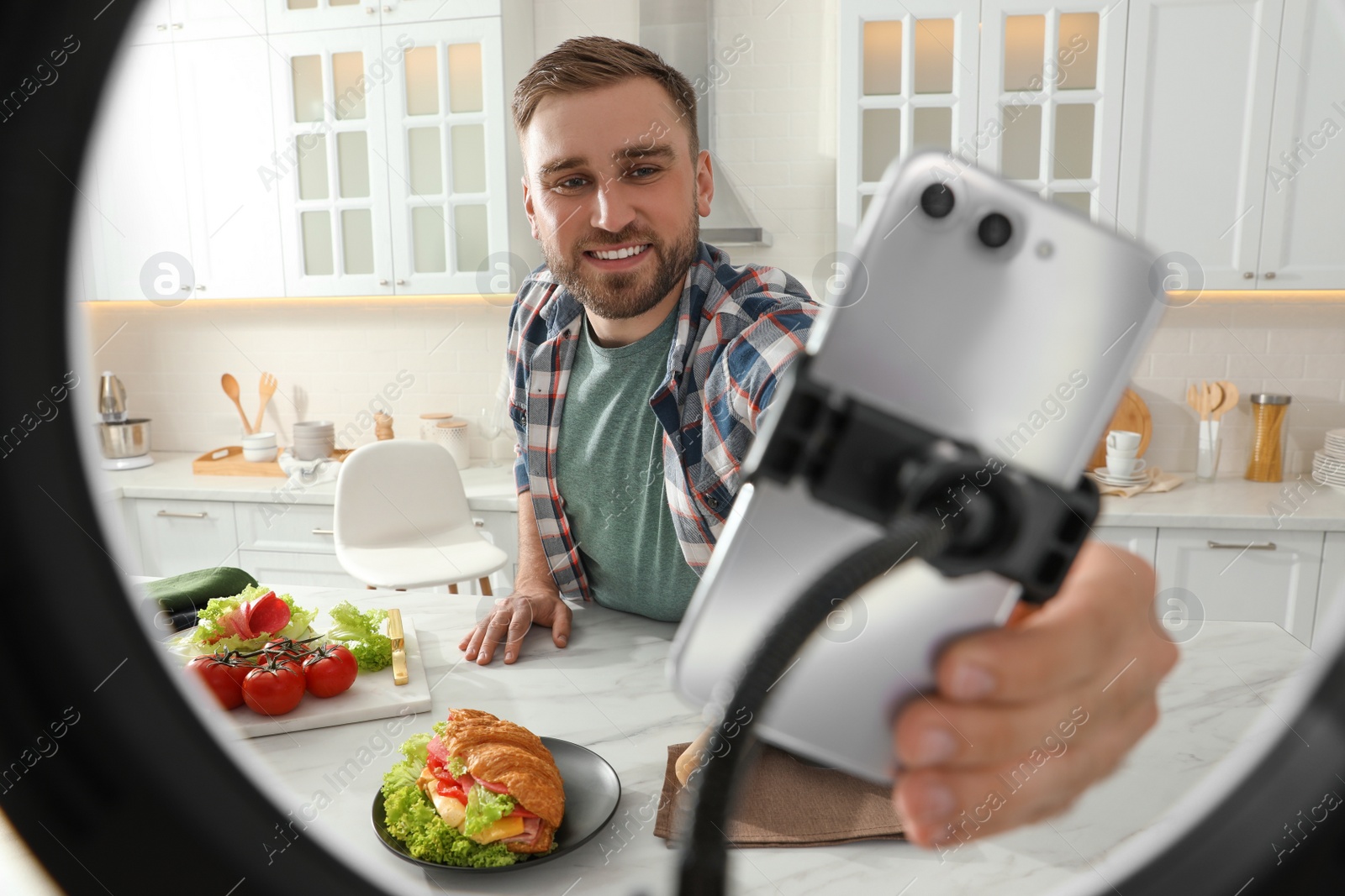 Photo of Blogger preparing for video recording in kitchen at home. Using smartphone and ring lamp