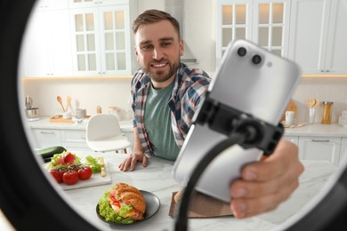 Blogger preparing for video recording in kitchen at home. Using smartphone and ring lamp