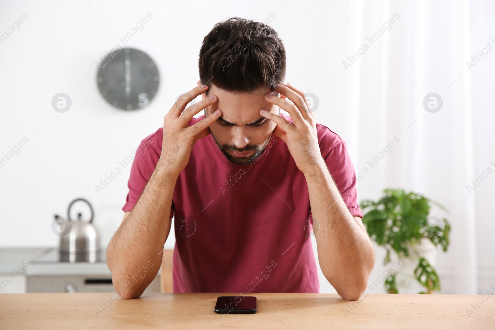 Photo of Young man addicted to smartphone at wooden table indoors