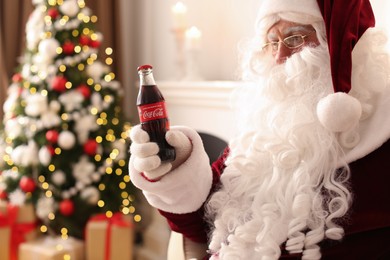 MYKOLAIV, UKRAINE - JANUARY 18, 2021: Santa Claus holding Coca-Cola bottle in room decorated for Christmas