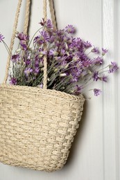 Stylish beach bag with beautiful bouquet of wildflowers hanging on white wooden door