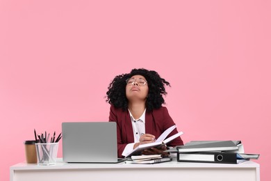 Photo of Stressful deadline. Exhausted woman sitting at white desk against pink background