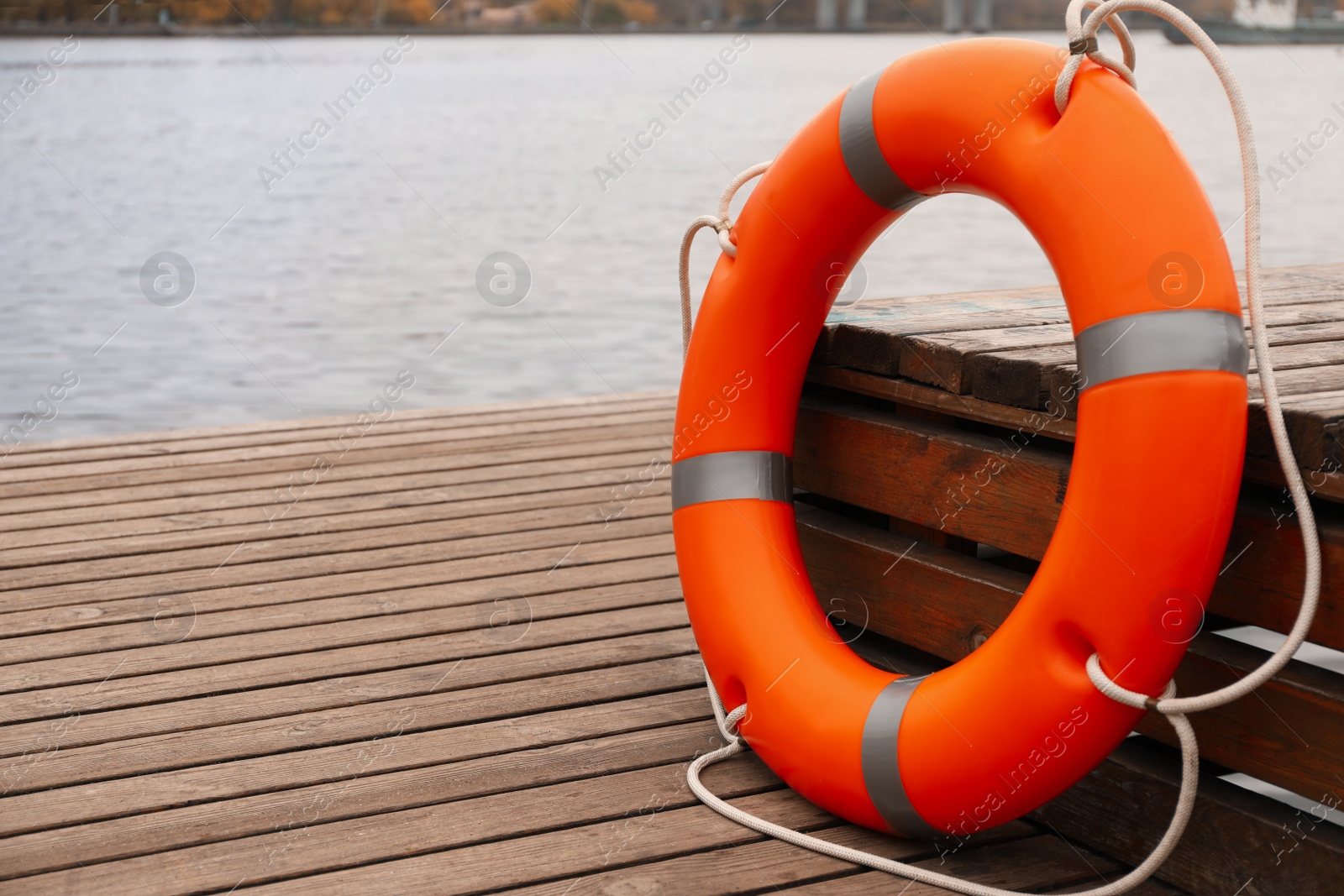 Photo of Orange lifebuoy on wooden pier near water. Rescue equipment