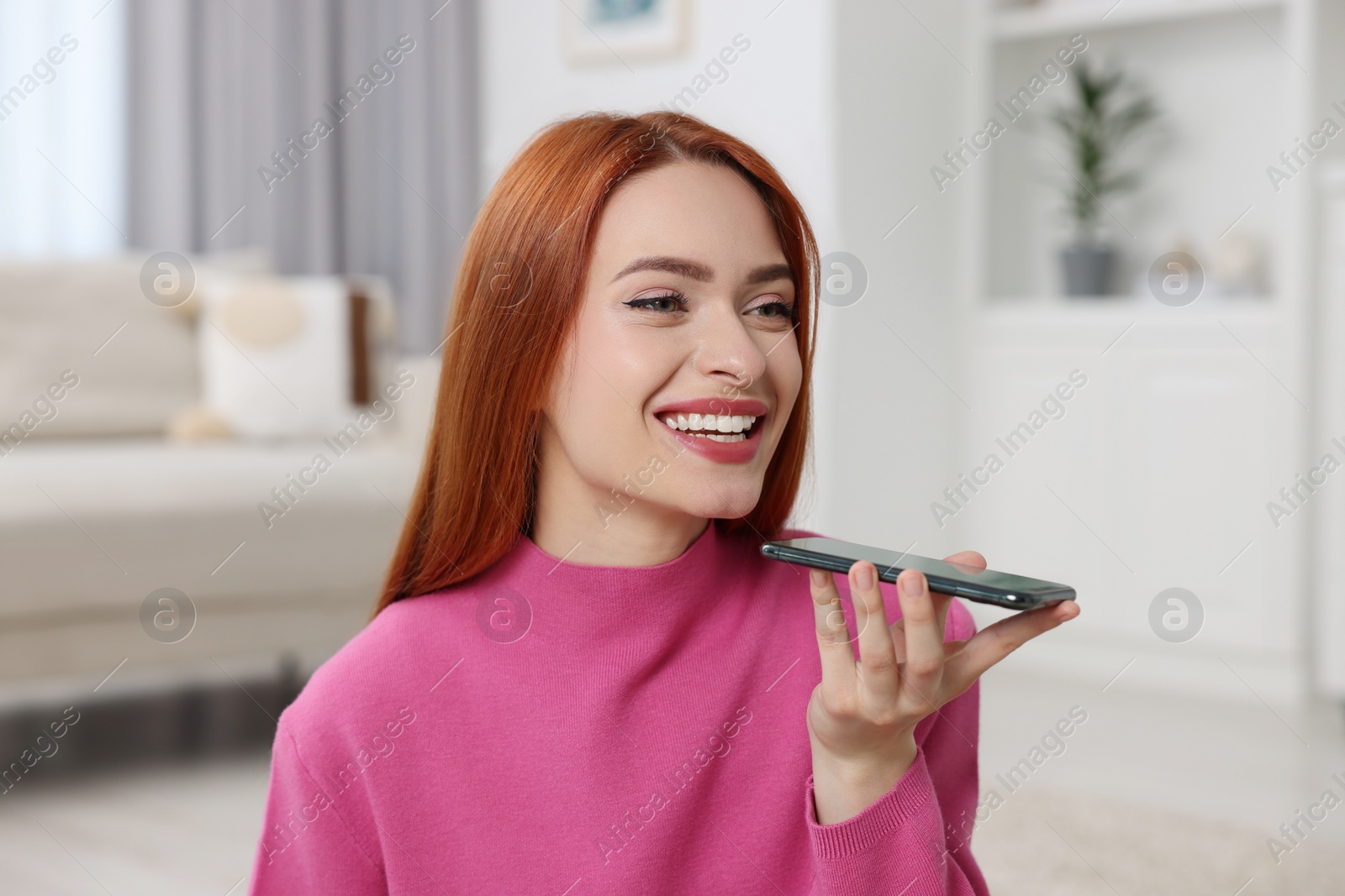 Photo of Happy woman sending voice message via smartphone at home