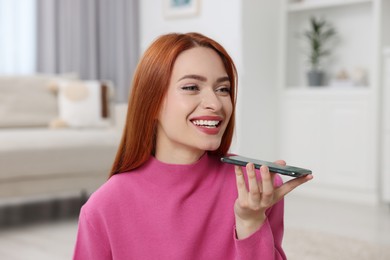 Happy woman sending voice message via smartphone at home