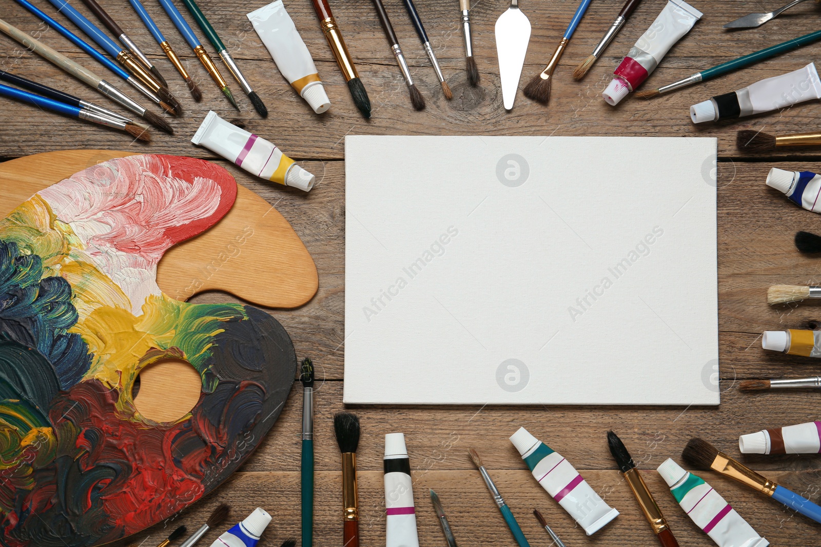 Photo of Blank canvas, brushes, paints and palette on wooden table, flat lay. space for text