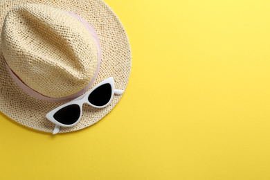 Photo of Women's sunglasses and hat on yellow background, top view. Space for text